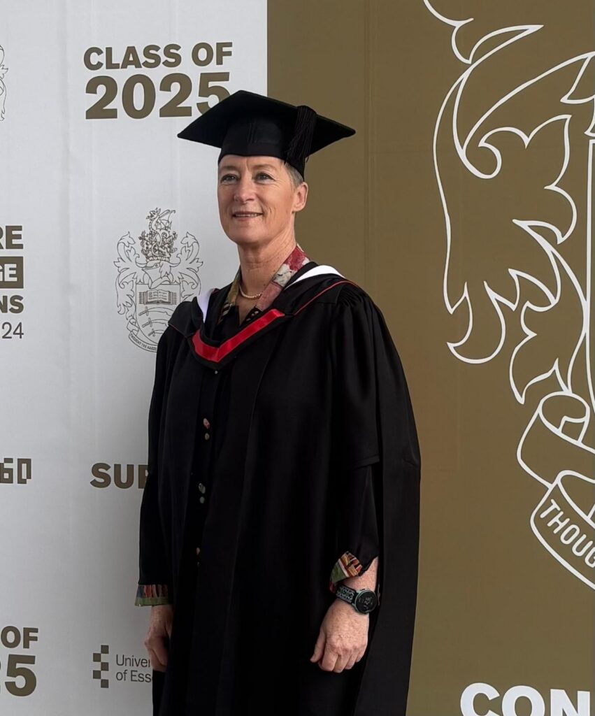 Zoe wearing a graduation robe and mortar board against a background with "class of 2025" and the coat of arms of university of essex